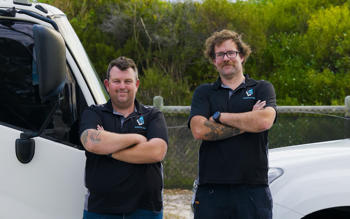 Brent and a Westplumb plumber, arms crossed, between the work truck and the ute